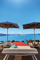 Un espacio de relax en la playa con dos tumbonas, una manta roja y dos sombrillas.