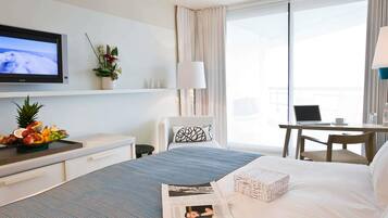 Habitación de hotel con cama, televisor, escritorio y ordenador portátil, y vistas al exterior.