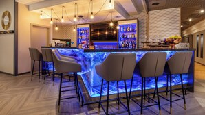 A bar area with a marble countertop, bar stools, hanging light fixtures, and shelves stocked with bottles. - Leonardo Hotel Verona (Verona)