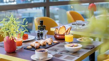 A breakfast table with croissants, a bowl of cereal, a glass of orange juice, and a vase with flowers.