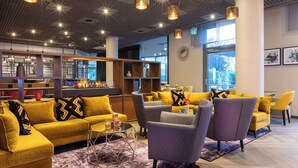 A modern lobby with a yellow sofa, patterned armchairs, and a bar area. - Leonardo Hotel Verona (Verona)