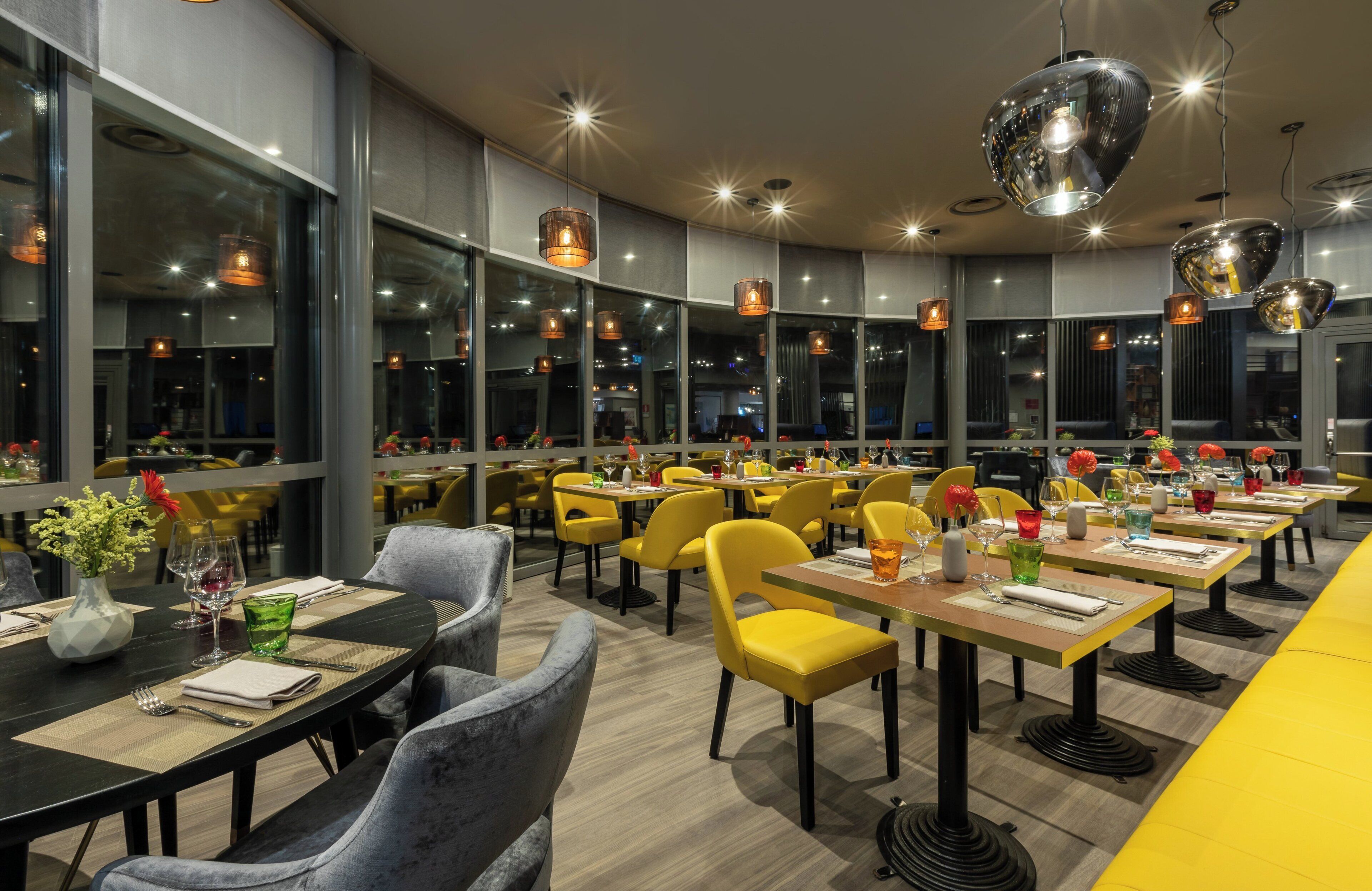 A modern restaurant with yellow chairs, black tables, and large windows.