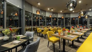 Ein modernes Restaurant mit gelben Stühlen, schwarzen Tischen und großen Fenstern.
