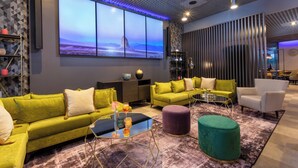 A modern living room with a large wall-mounted TV, green sofas, a coffee table, and a patterned rug. - Leonardo Hotel Verona (Verona)