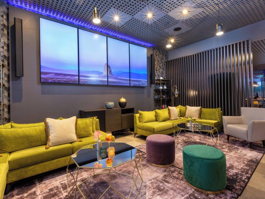 A modern living room with a large wall-mounted TV, green sofas, a coffee table, and a patterned rug.