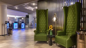 A lobby with green upholstered armchairs, a reception desk, and a modern chandelier. - Leonardo Hotel Verona (Verona)