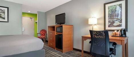 Habitación de hotel con cama, escritorio con silla, televisor, lámpara y un cuadro en la pared.