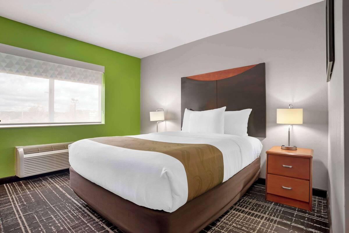 A hotel room with a bed, bedside tables, and a window with blinds.