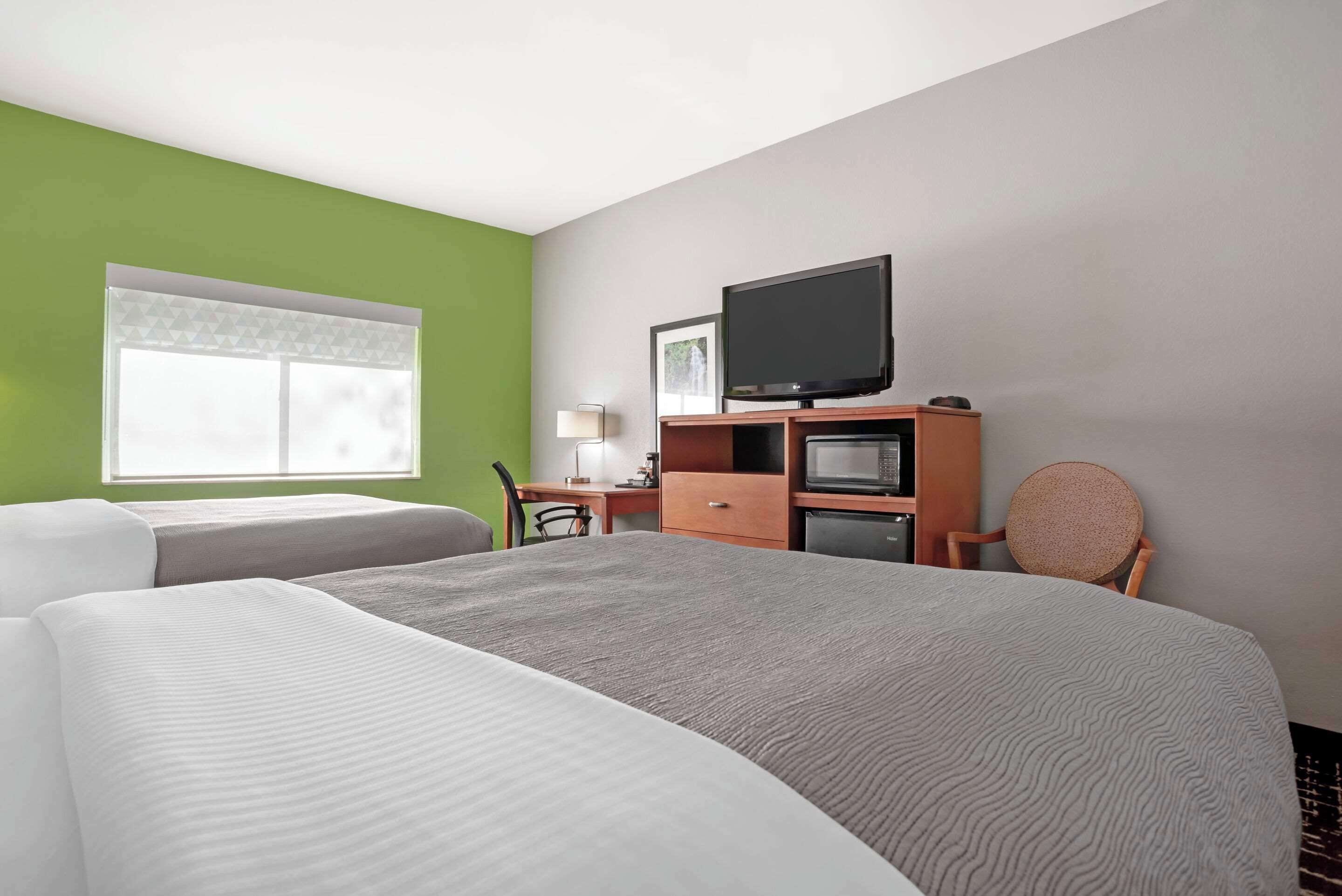 A hotel room with two beds, a desk with a computer, a television, and a chair.