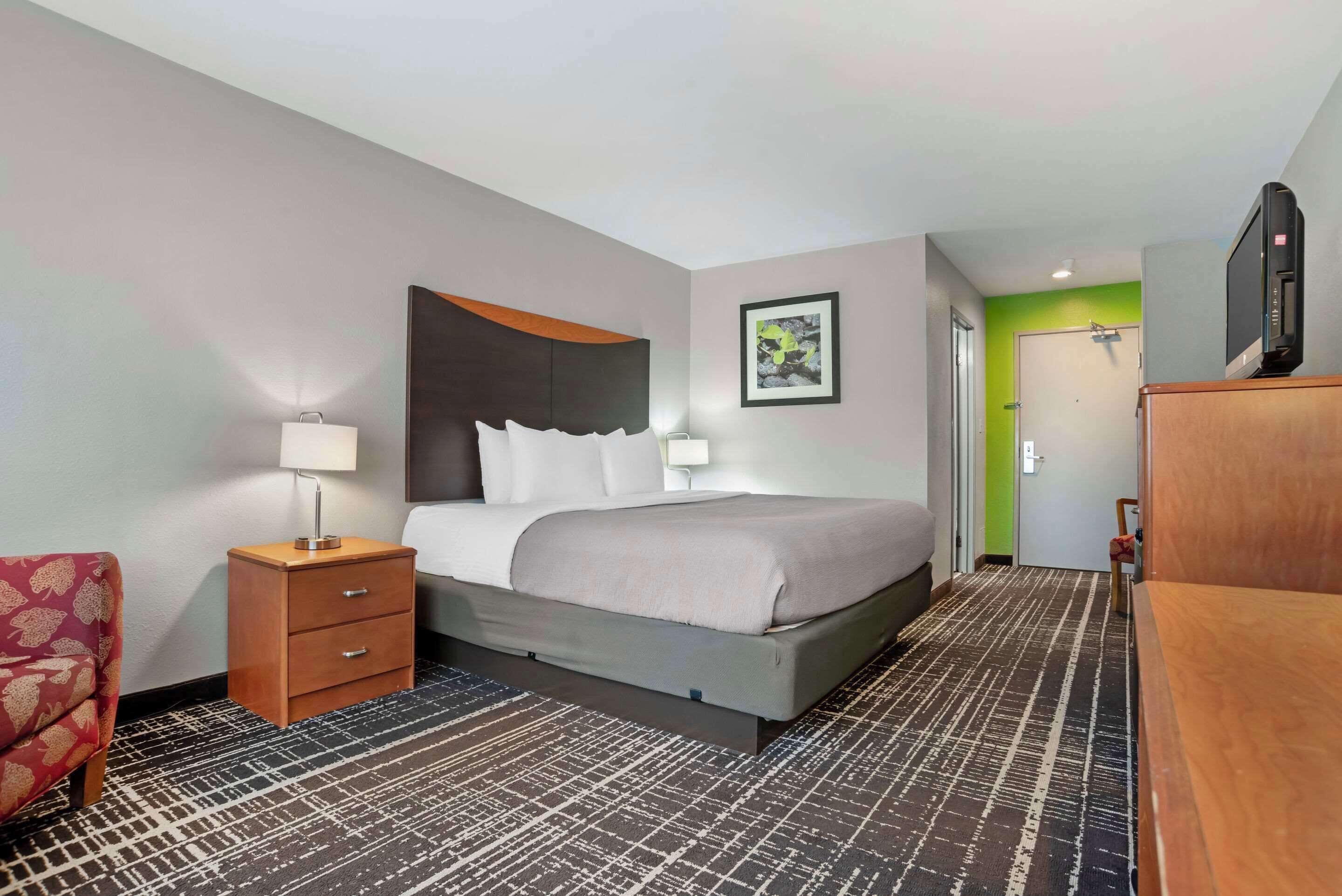 A hotel room with a bed, a nightstand, a chair, a desk, a television, and a door.