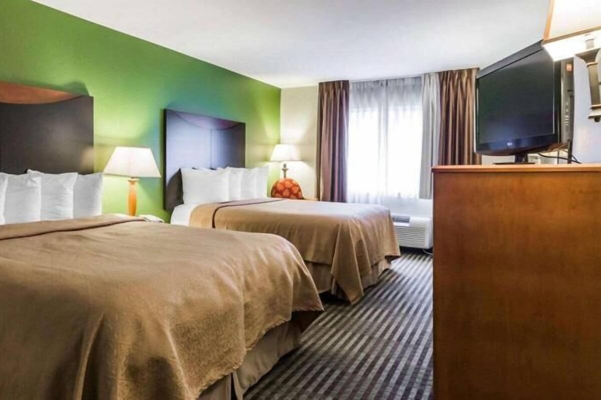A hotel room with two beds, a television, a desk, and a window with curtains.