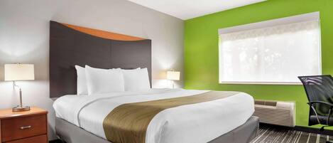 Una habitación de hotel con una cama grande, una mesita de noche, una lámpara, una silla y una ventana con persianas.