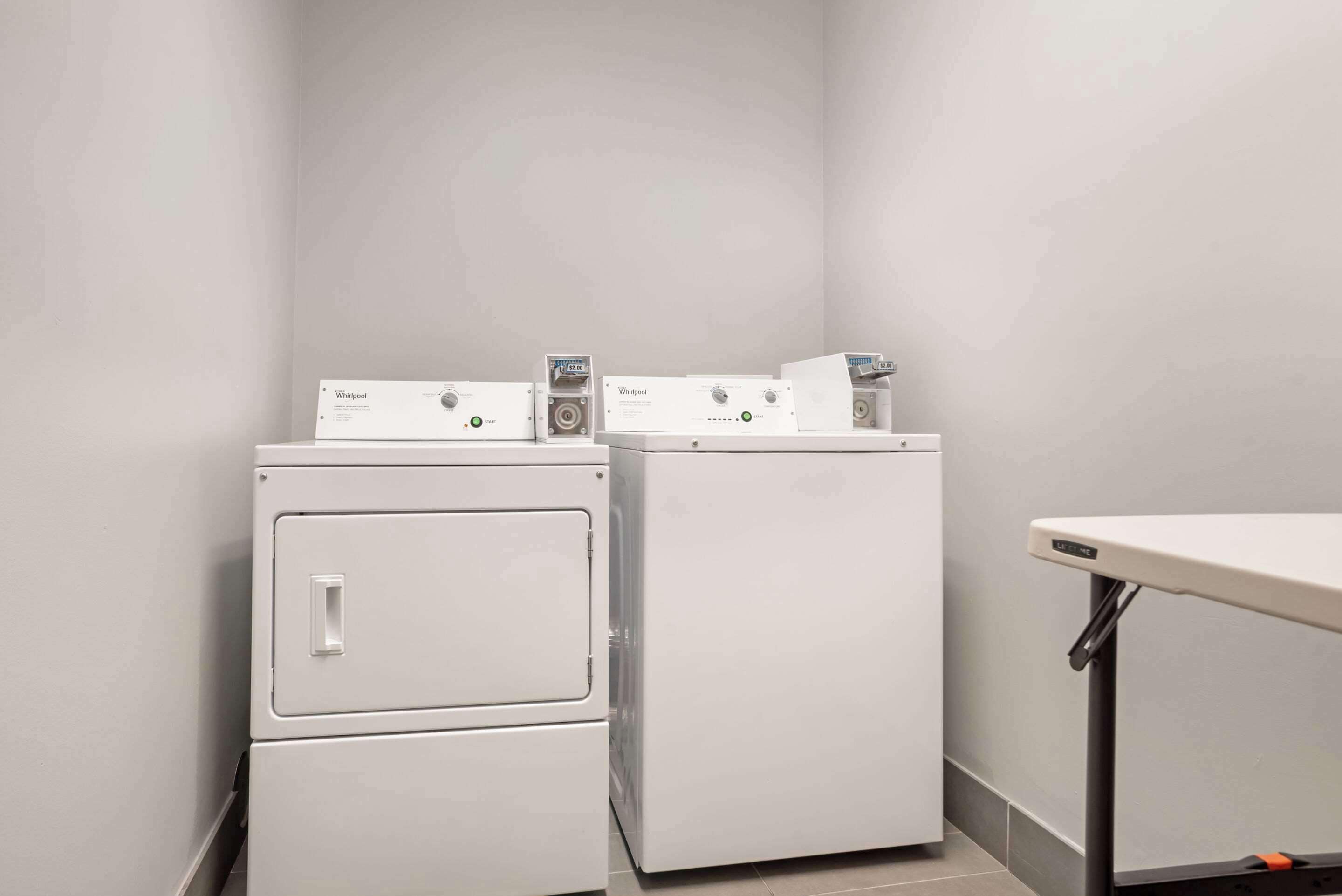 A laundry area with two stacked washers and dryers, a table, and a wall-mounted control panel.