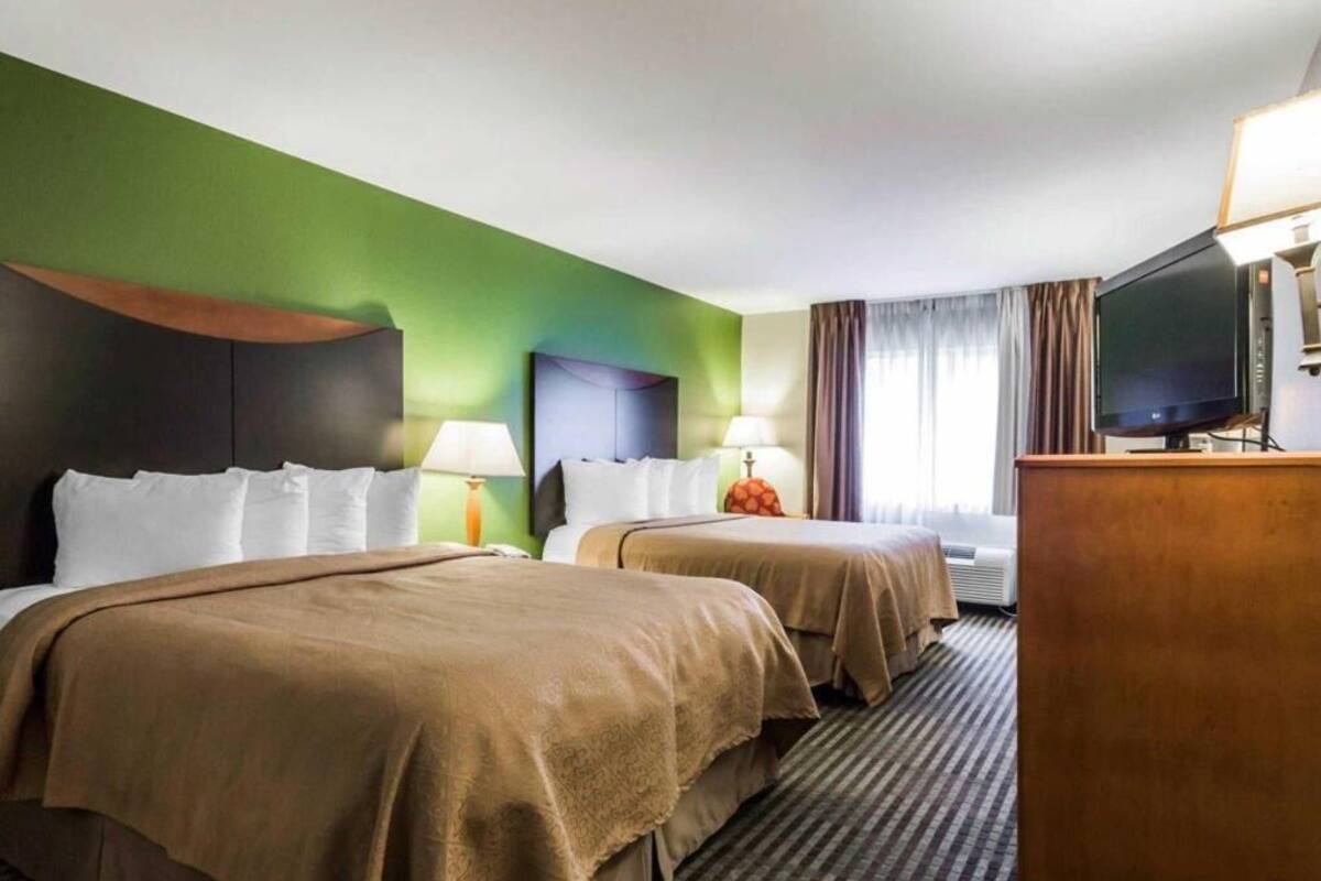 A hotel room with two beds, a television, and a desk.