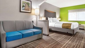 A hotel room with a grey sofa, a bed with white bedding, a green accent wall, and a framed picture of a bridge. - Quality Inn & Suites Birmingham - Highway 280 (Birmingham)