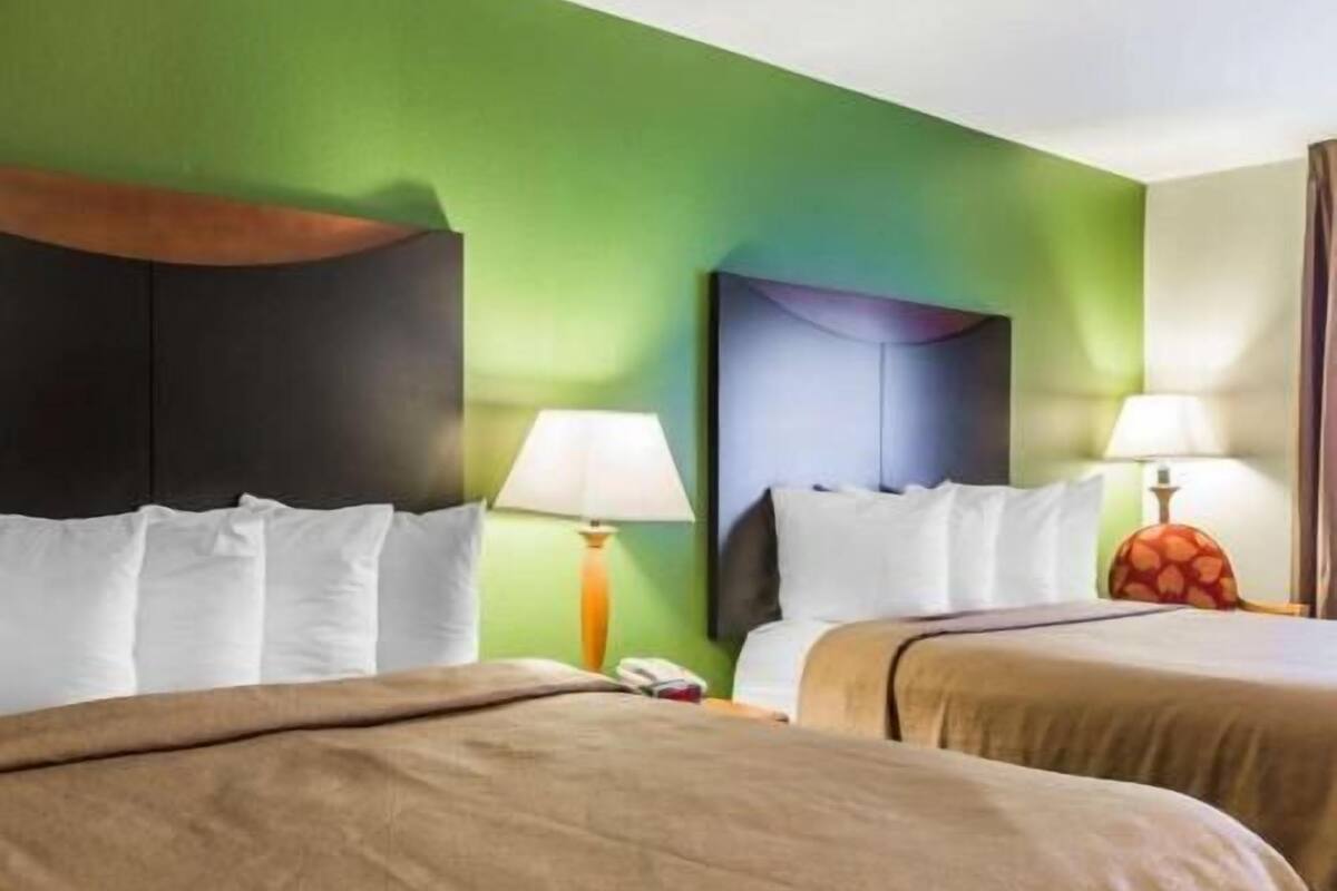 A hotel room with two beds, a green wall, and two bedside lamps.