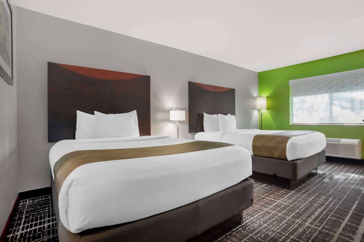 A hotel room with two beds, a green accent wall, and a large window.