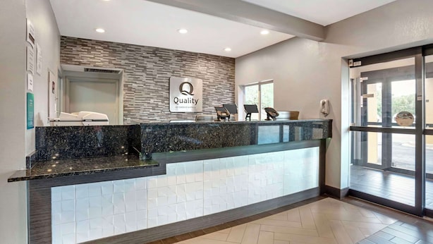 A hotel reception area with a marble counter, a 'Quality by Choice Hotels' sign, a reception desk, and a glass door entrance. - Quality Inn & Suites Birmingham - Highway 280 (Birmingham)