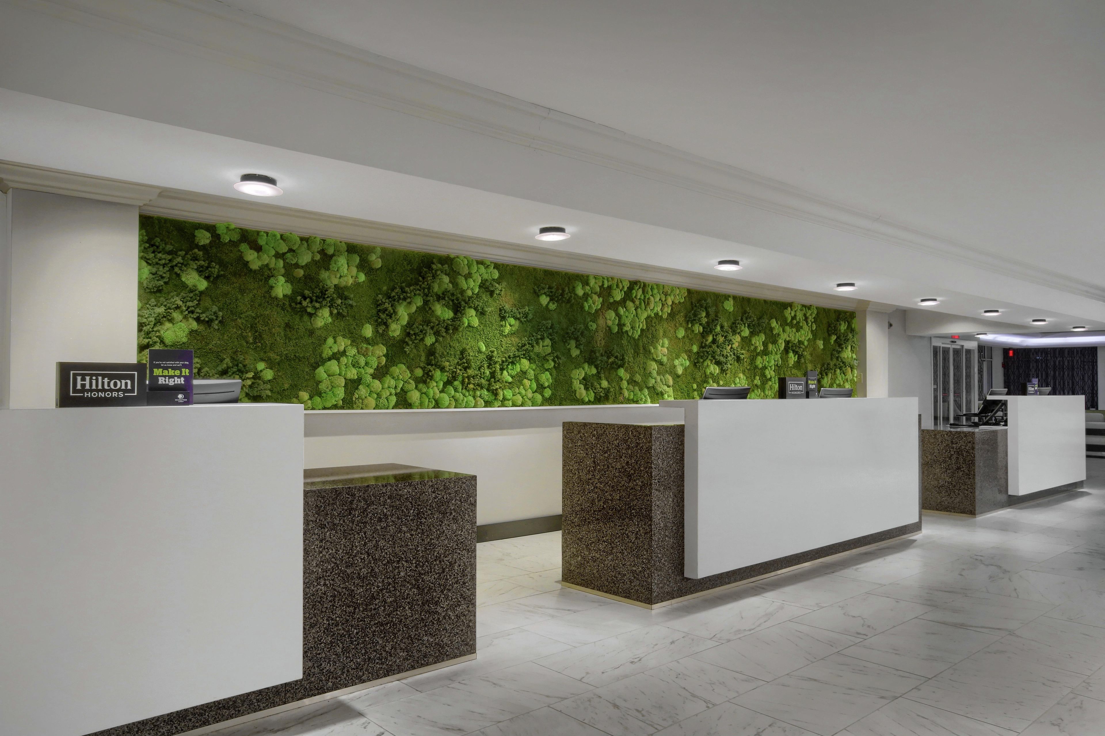 A hotel reception area with a green wall, multiple reception counters, and a clean, modern design.