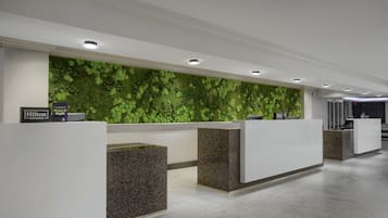 A hotel reception area with a green wall, multiple reception counters, and a clean, modern design.