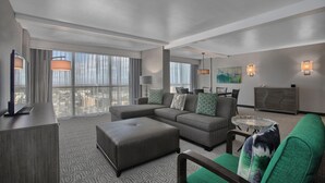 A modern hotel room with a sectional sofa, a flat-screen TV, a large window with curtains, a dining table, and a radiator. - DoubleTree by Hilton at the Entrance to Universal Orlando (Orlando)