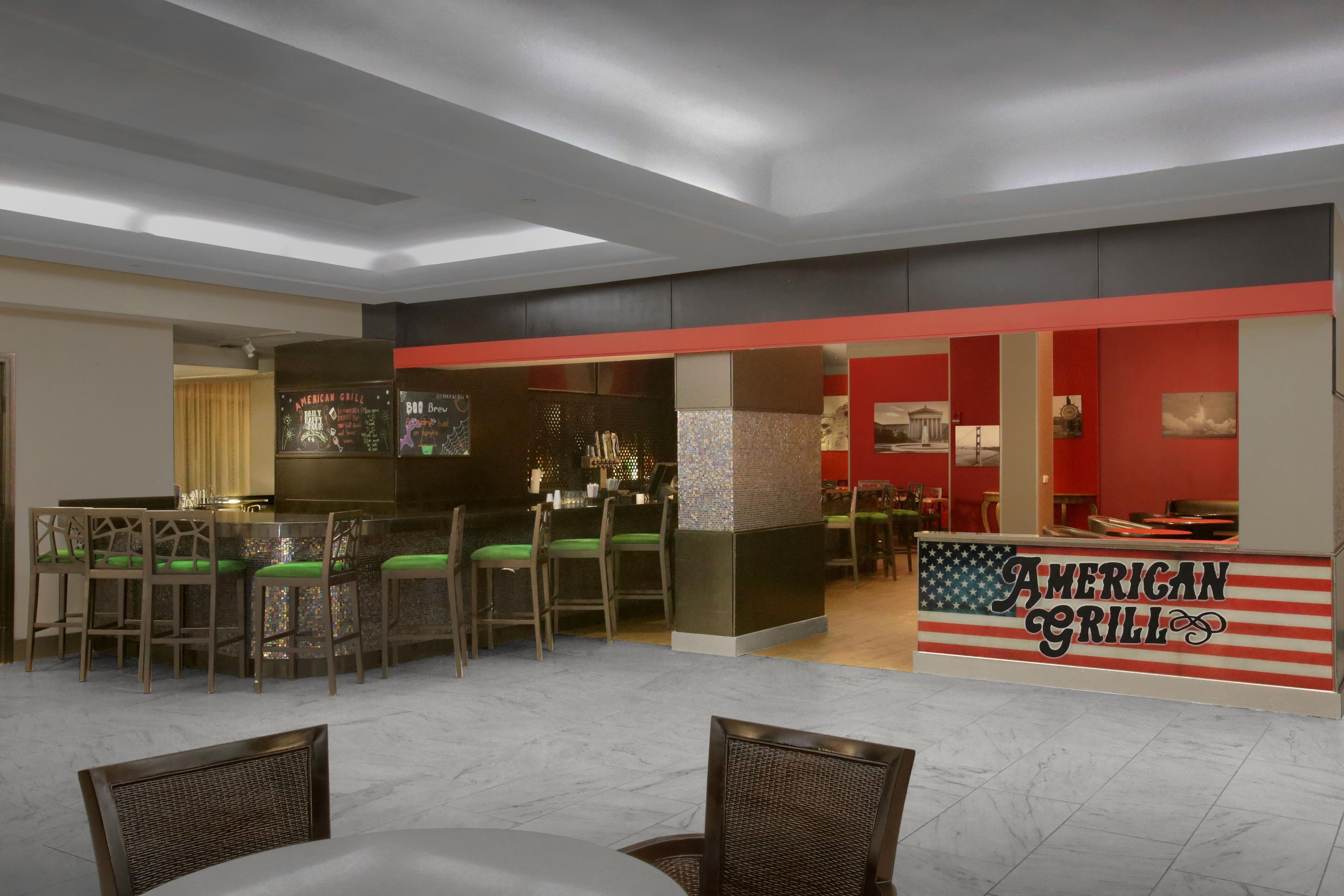 Ein Restaurantinneres mit Barbereich, Sitzgelegenheiten und einem Schild mit der Aufschrift 'AMERICAN GRILL'.