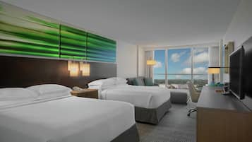 Habitación de hotel con dos camas, un escritorio, un televisor y un ventanal con vistas.