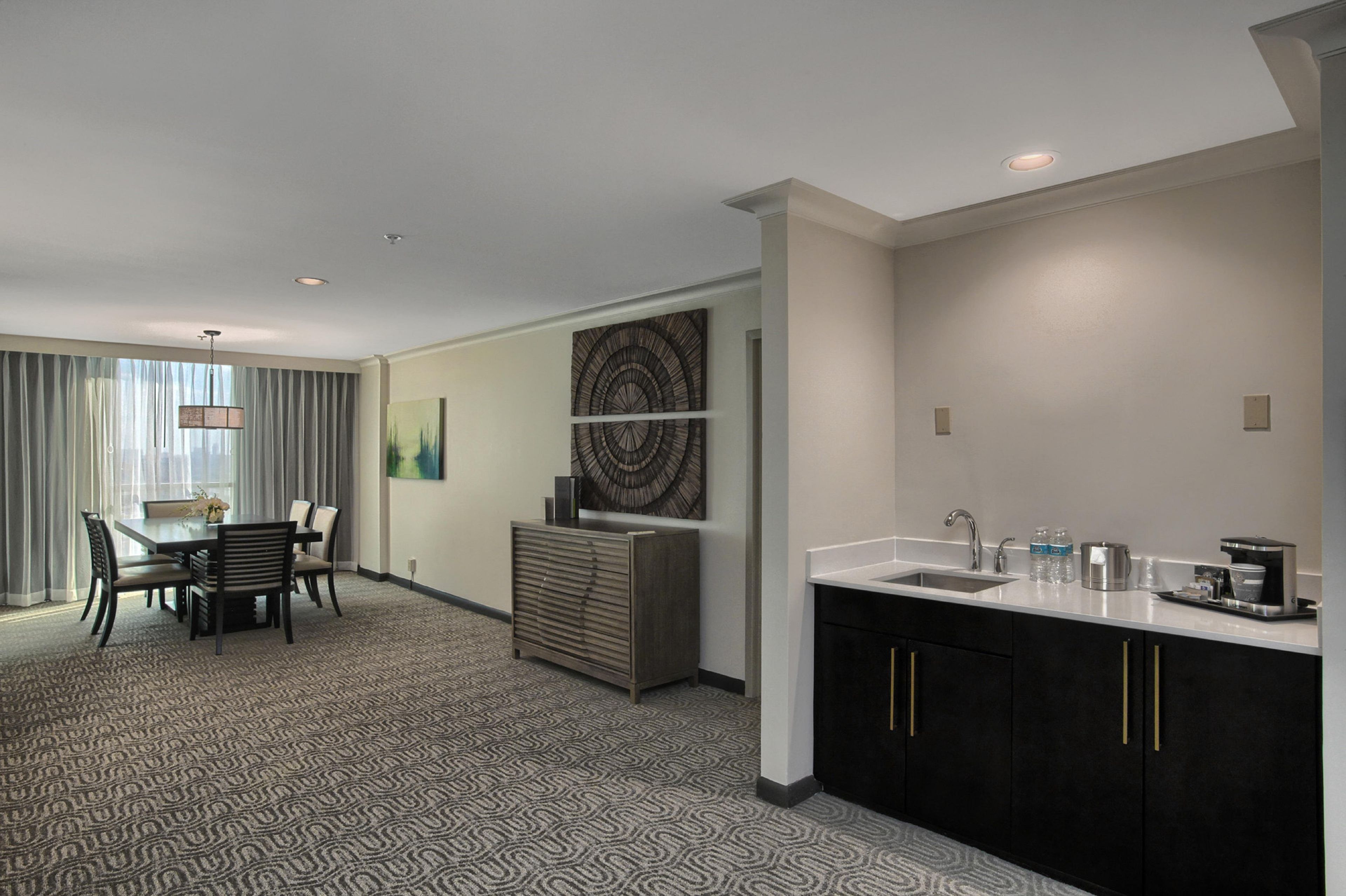 A hotel room with a dining area, a kitchenette, and a large window with curtains.
