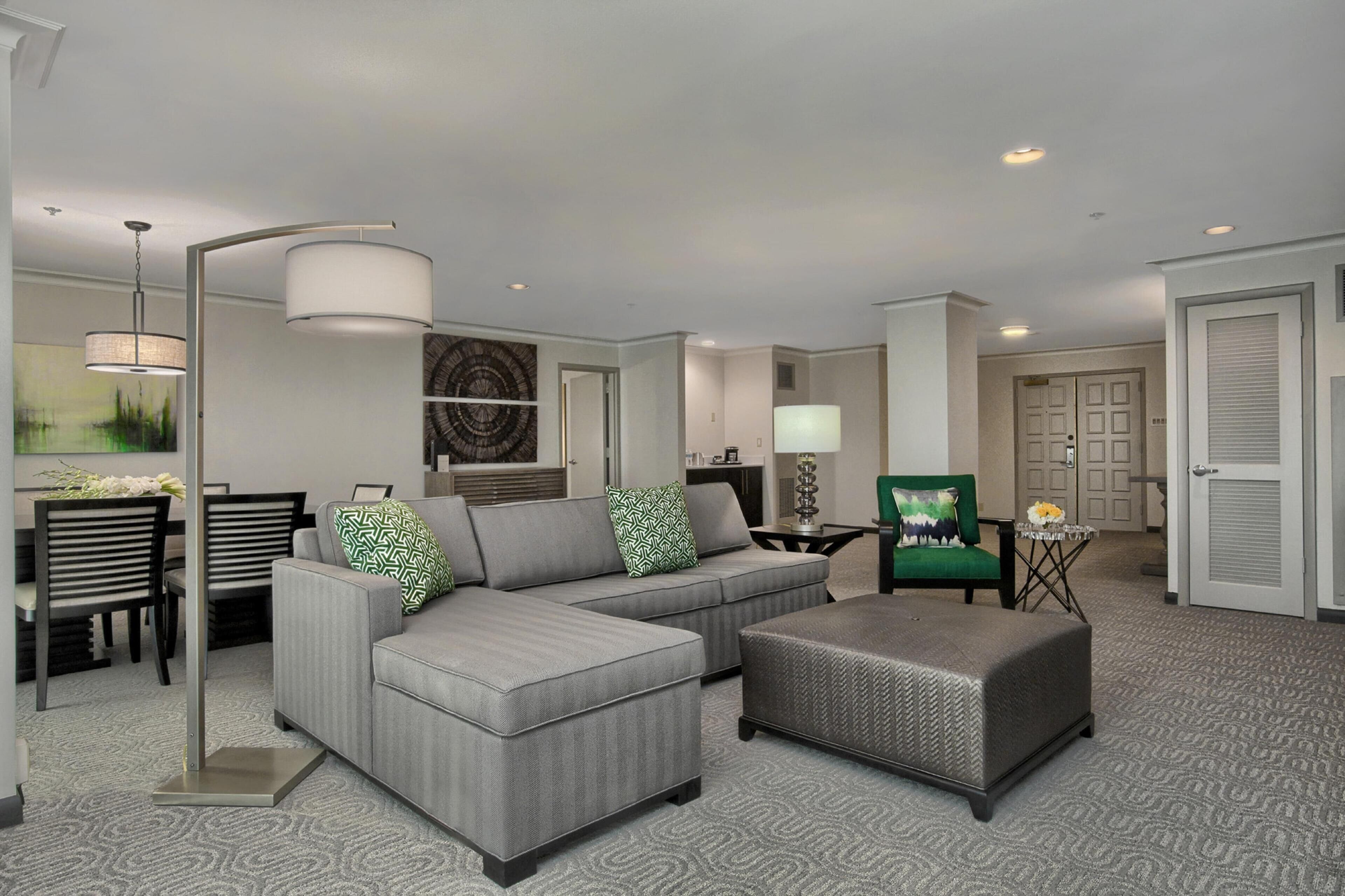 A modern living room with a sectional sofa, ottoman, and a dining area with chairs and a table.