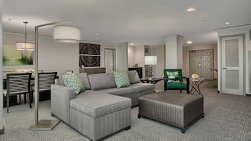 Ein modernes Wohnzimmer mit einem Ecksofa, einem grünen Sessel, einer Essecke mit Tisch und Stühlen sowie einem Flur zu einer Tür.