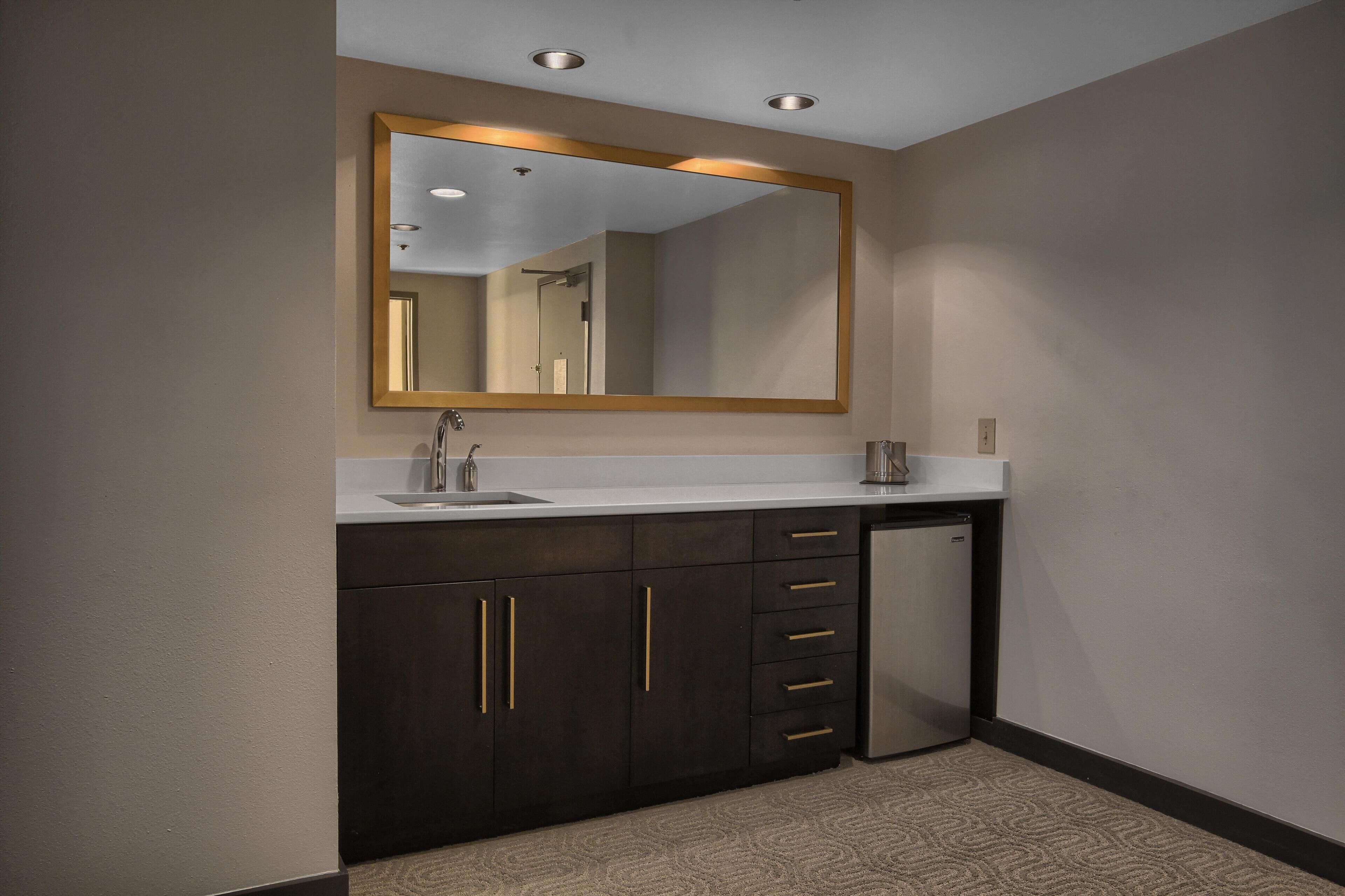 Une salle de bain moderne avec un grand miroir, des meubles de rangement aux couleurs sombres, un lavabo et un lave-vaisselle compact.