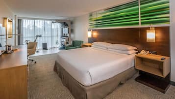 A hotel room with a large bed, a desk, a chair, a desk lamp, a phone, and a wall-mounted TV.