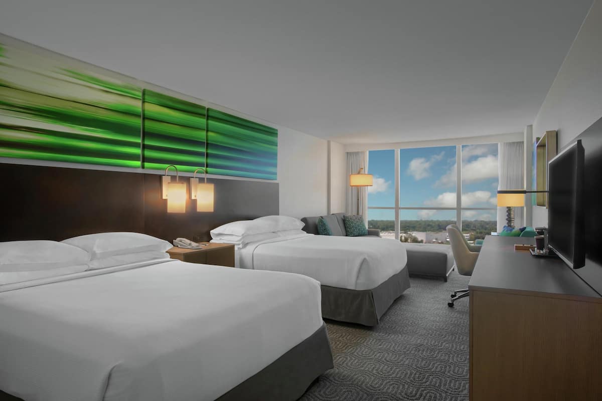 A hotel room with two beds, a desk, a TV, and a large window with a view.