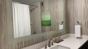 A bathroom with a large mirror, a shower, a sink, and a towel rack.