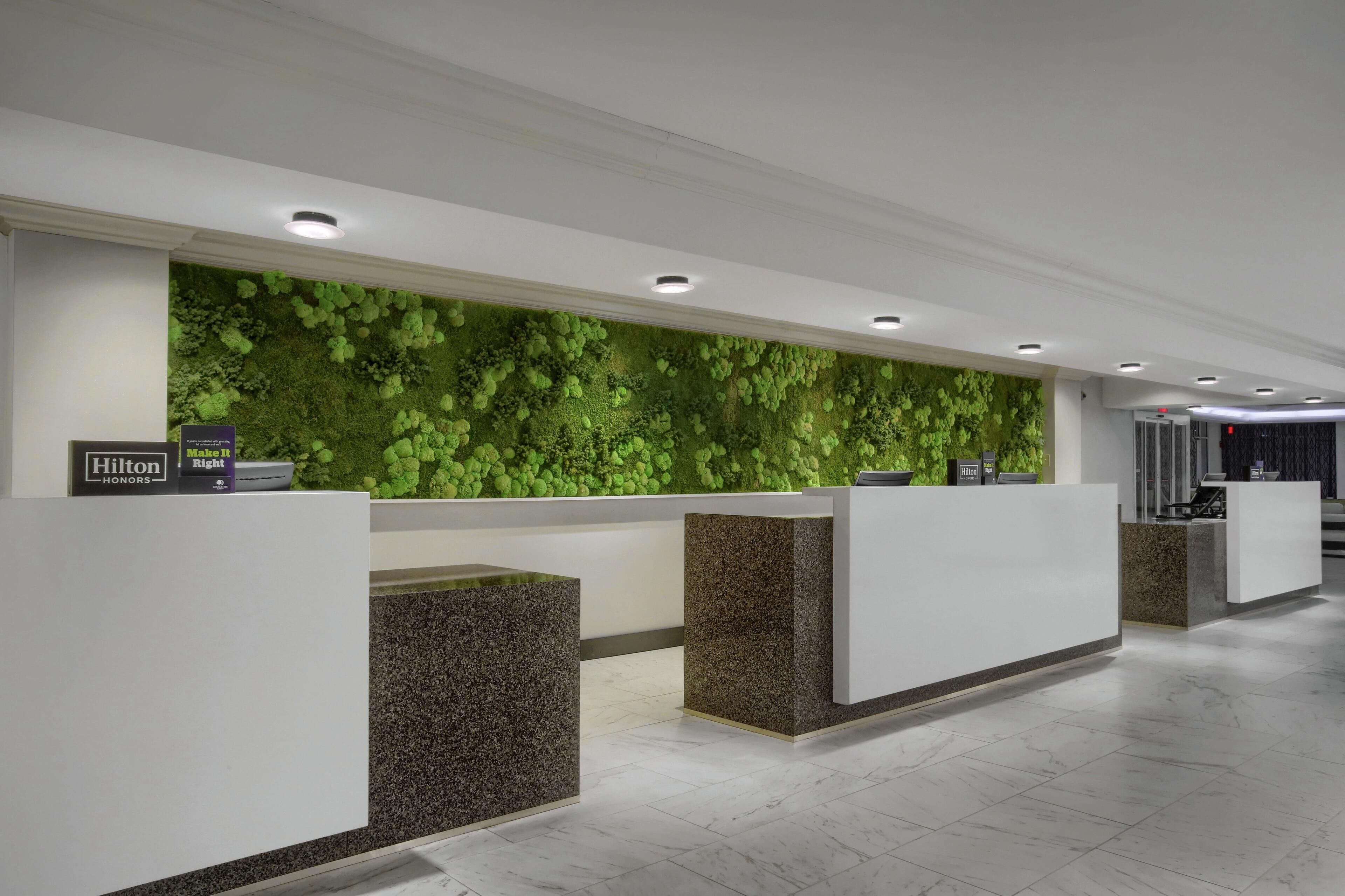 Zona de recepción de hotel con pared verde, varias mesas de recepción y un diseño limpio y moderno.
