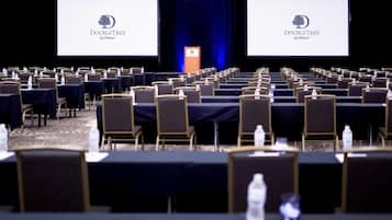 Un salón de conferencias con filas de mesas y sillas, un atril y dos pantallas que muestran el logotipo de DoubleTree by Hilton.