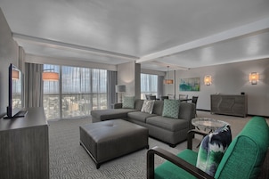 Een moderne hotelkamer met een modulaire bank, een klein voetenbankje, een glazen salontafel en een flatscreen televisie.