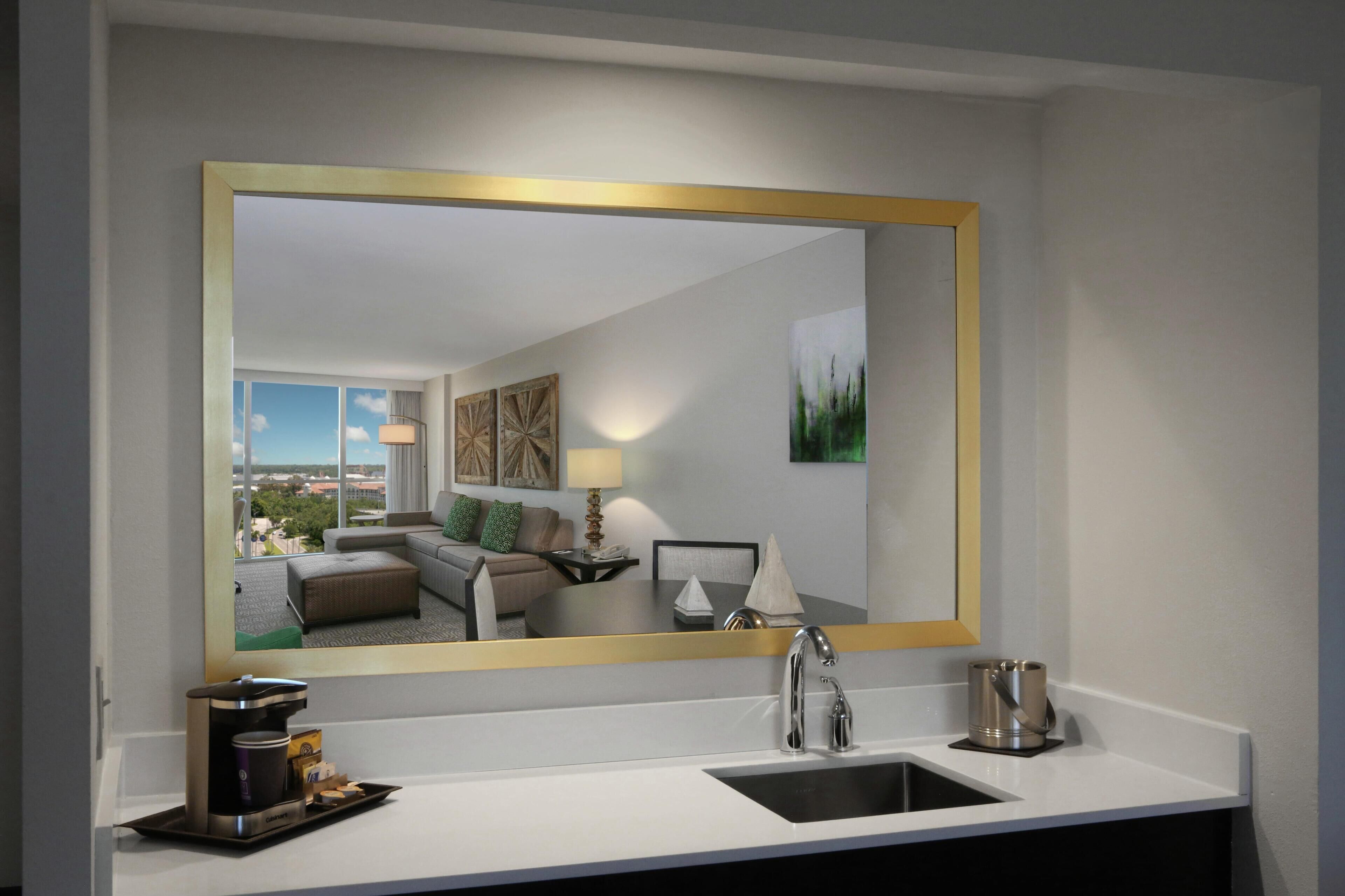 A hotel bathroom with a large mirror, a sink, a coffee maker, and a tray with toiletries.