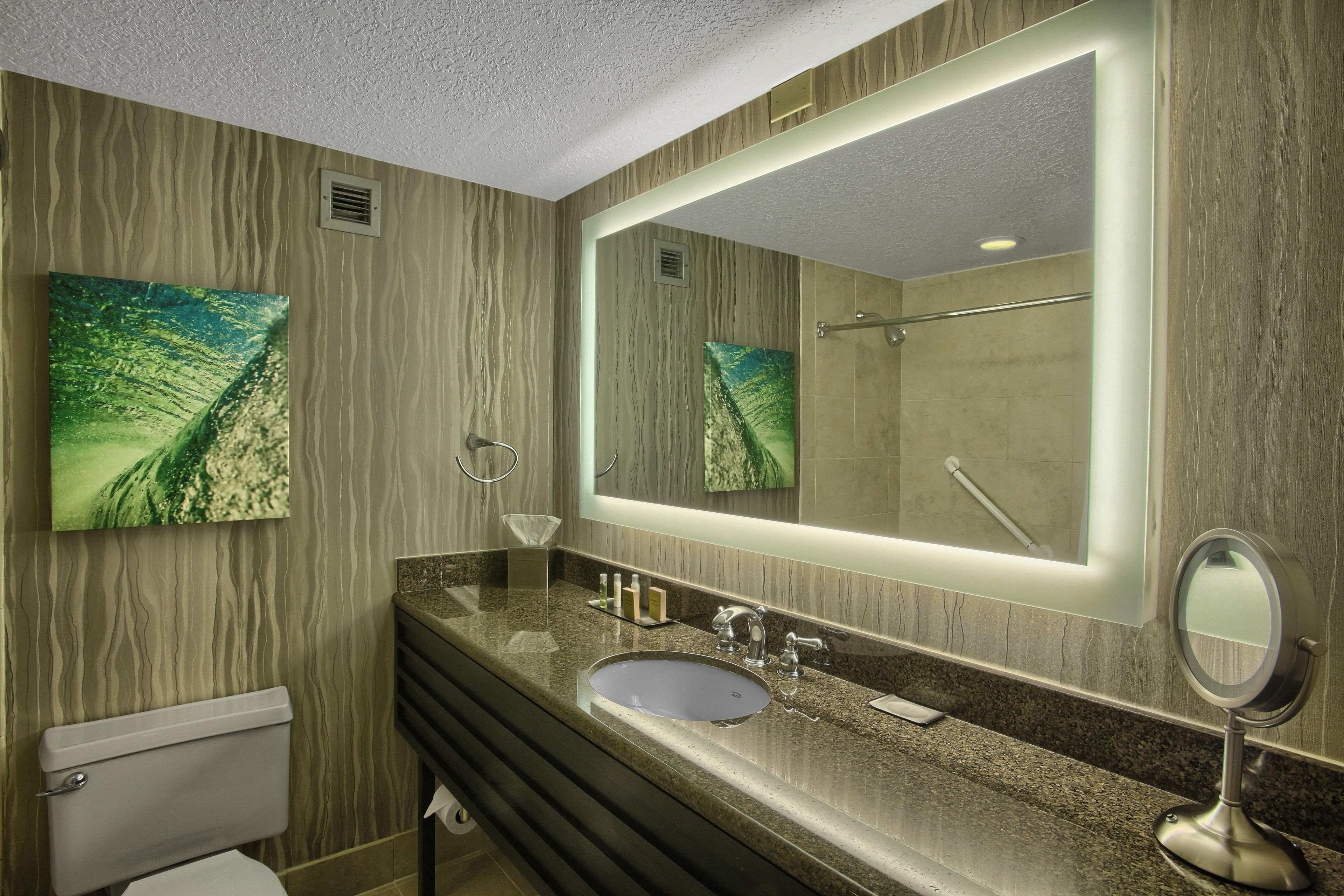 Een moderne badkamer met een granieten aanrechtblad, een grote spiegel en een toilet.