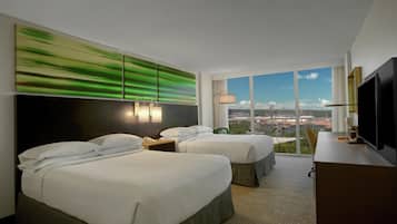 Habitación de hotel con dos camas, un ventanal con vistas a la ciudad, un televisor de pantalla plana y un cuadro abstracto moderno en la pared.