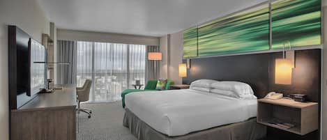 A hotel room with a bed, desk, chair, and a large window with curtains.