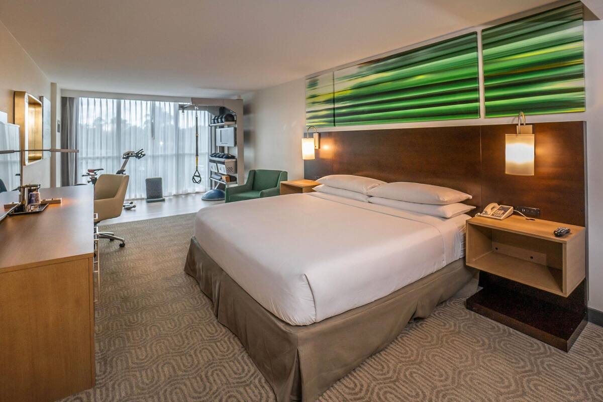A hotel room with a large bed, a desk, a chair, a nightstand, and a wall-mounted phone.
