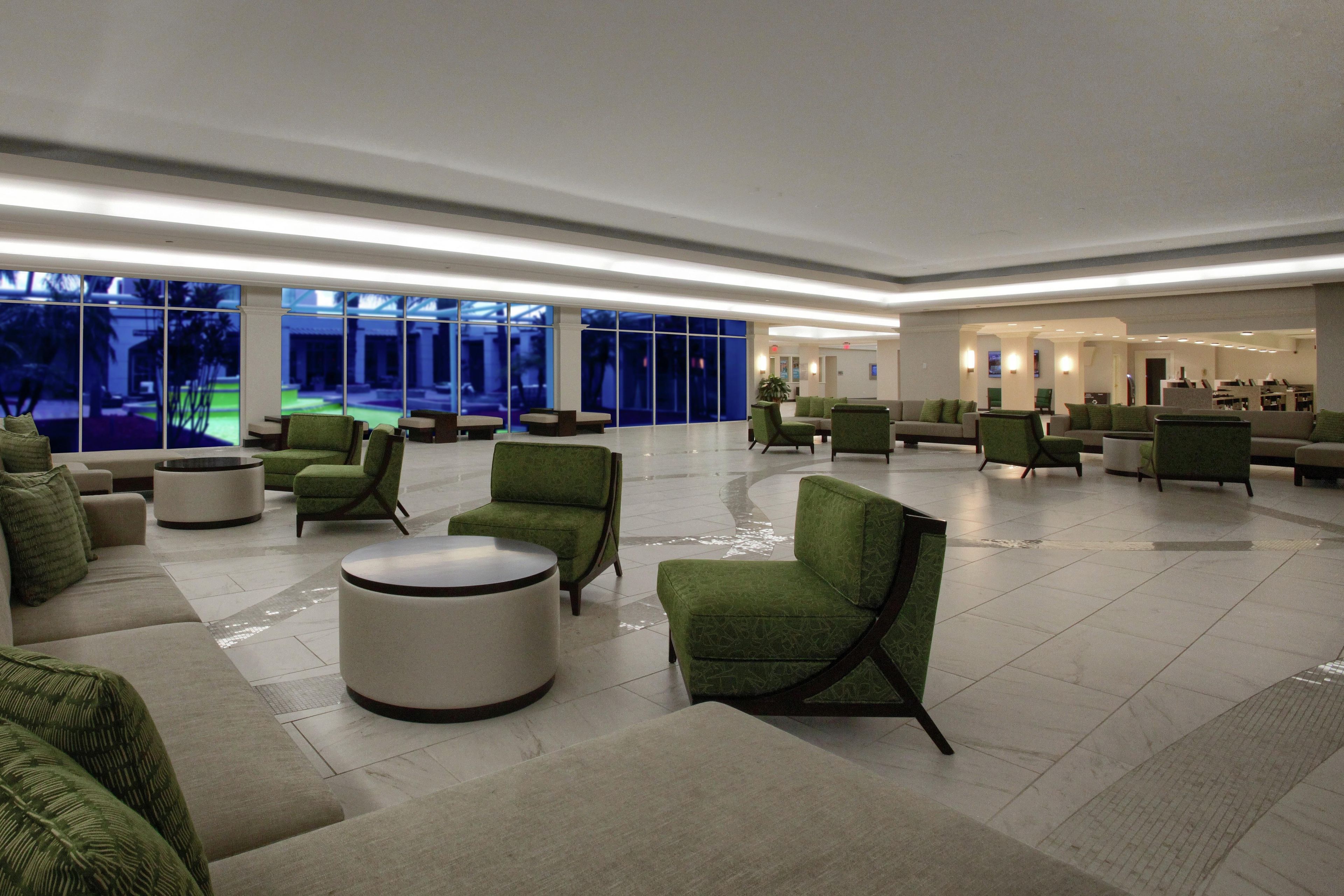 Eine großzügige Lobby mit grünen Polstersitzgelegenheiten, einem runden Couchtisch und Blick ins Freie durch große Fenster.