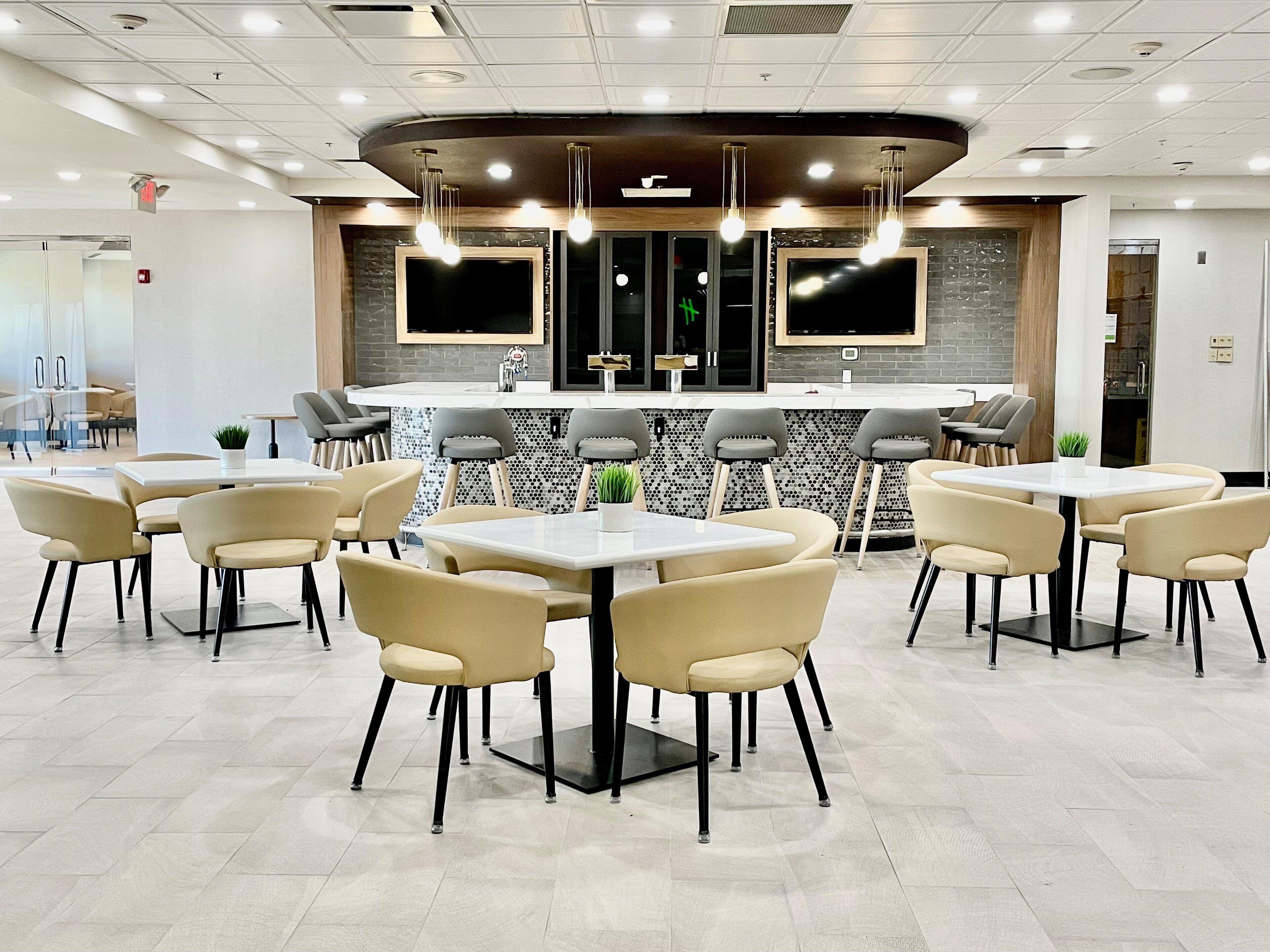 Un restaurante moderno con mesas redondas y taburetes de bar, una isla central con pileta y una pantalla grande sobre la barra.