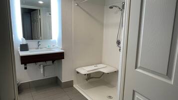 Un baño con lavamanos, espejo, ducha y toallero.