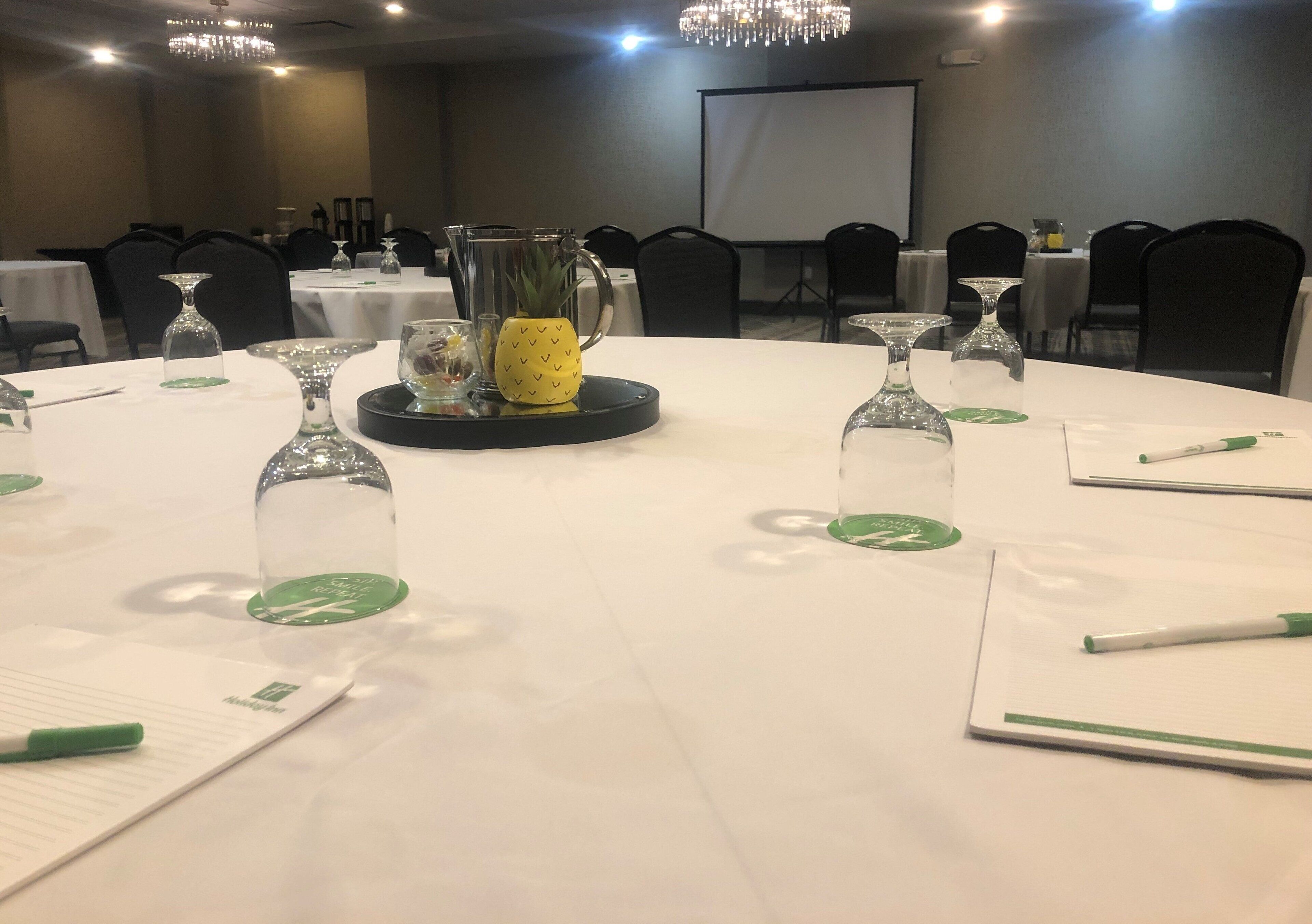 A conference room with round tables, each with a white tablecloth, glass candle holders, and a pineapple centerpiece.