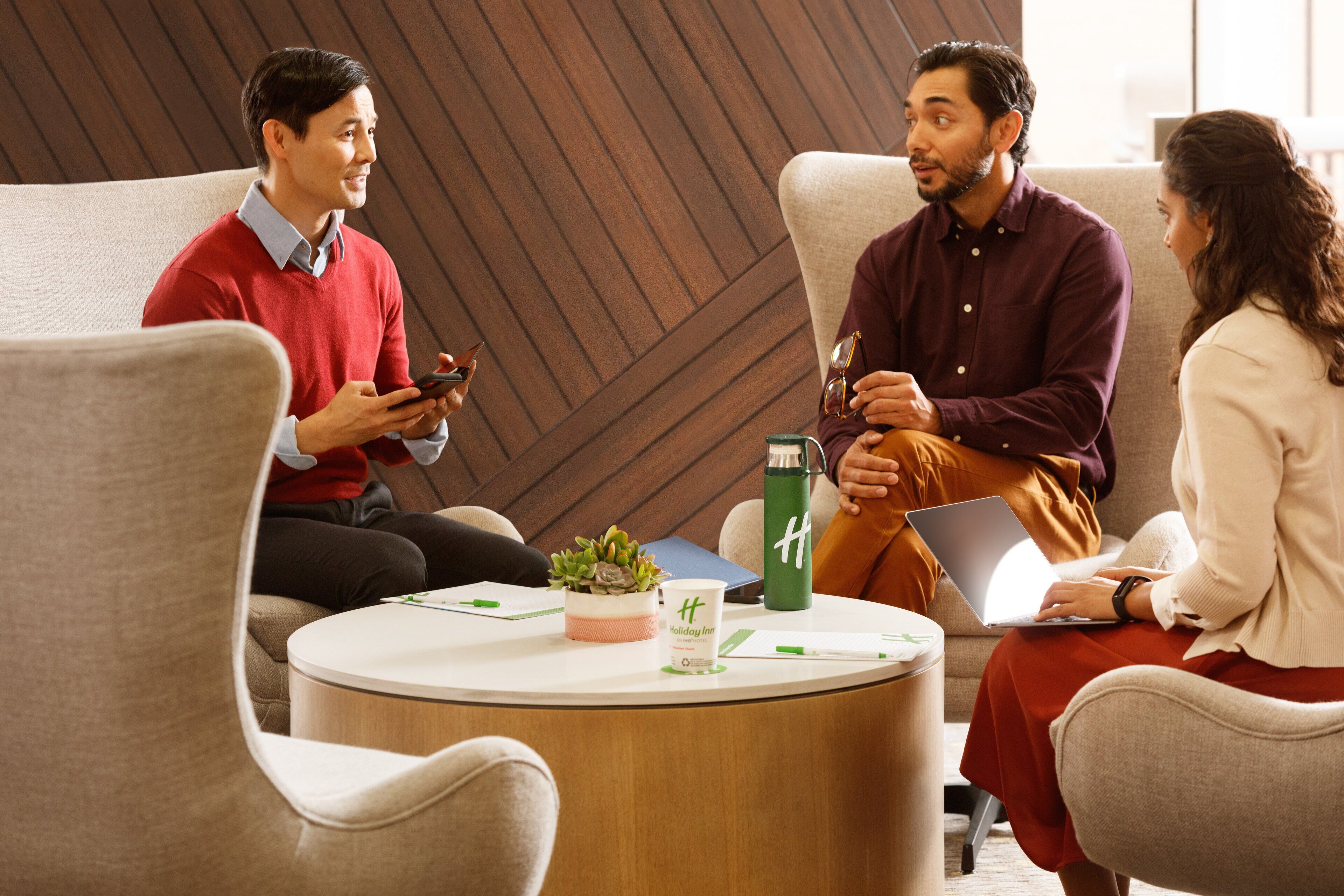 A group of people sitting around a round table in a modern room with a wooden accent wall.