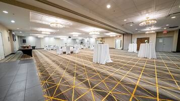 A spacious conference room with a patterned carpet, multiple tables with white tablecloths, and chandeliers on the ceiling.