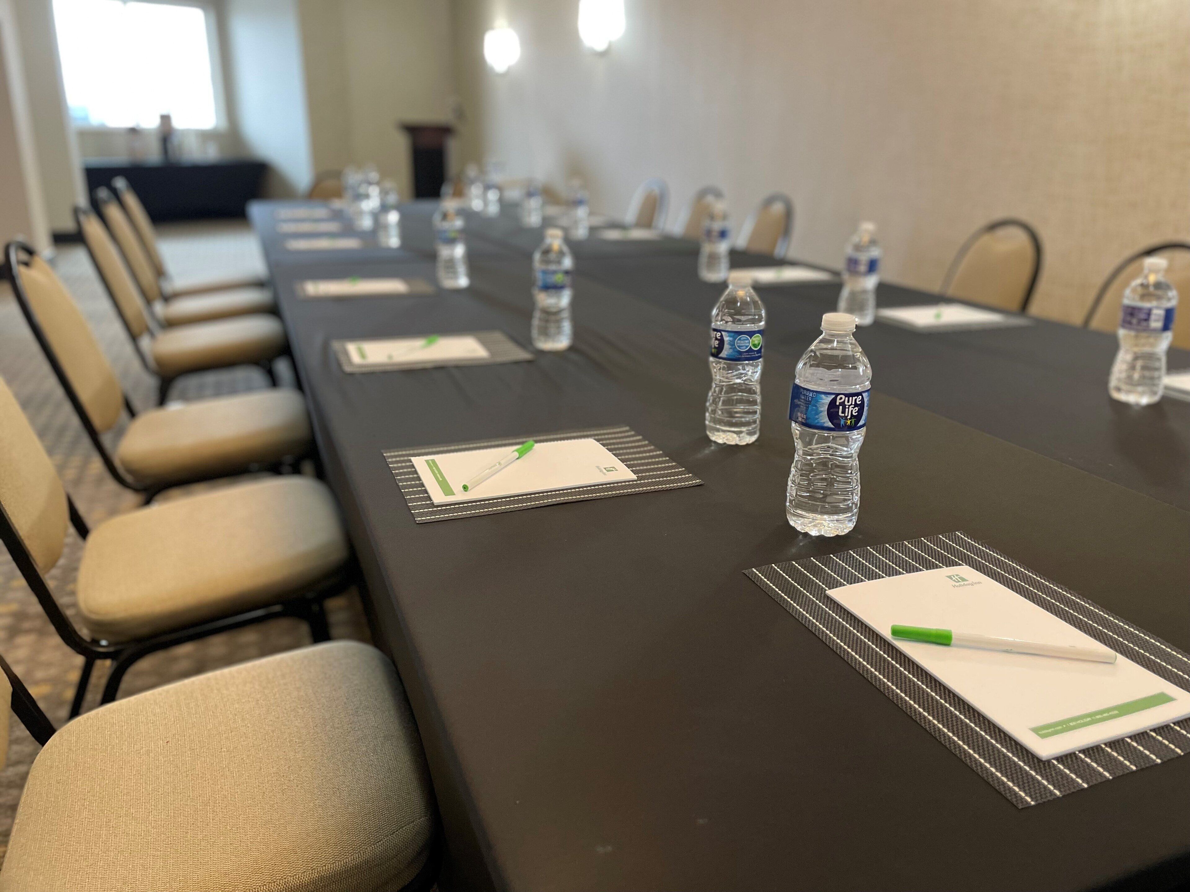 A conference room with a long table, chairs, nameplates, water bottles, and pens on place mats.