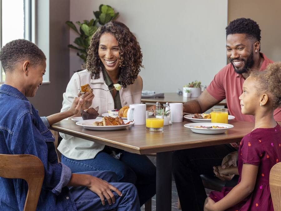 Eine Familie genießt ein Frühstück mit Speisen und Getränken an einem Tisch.